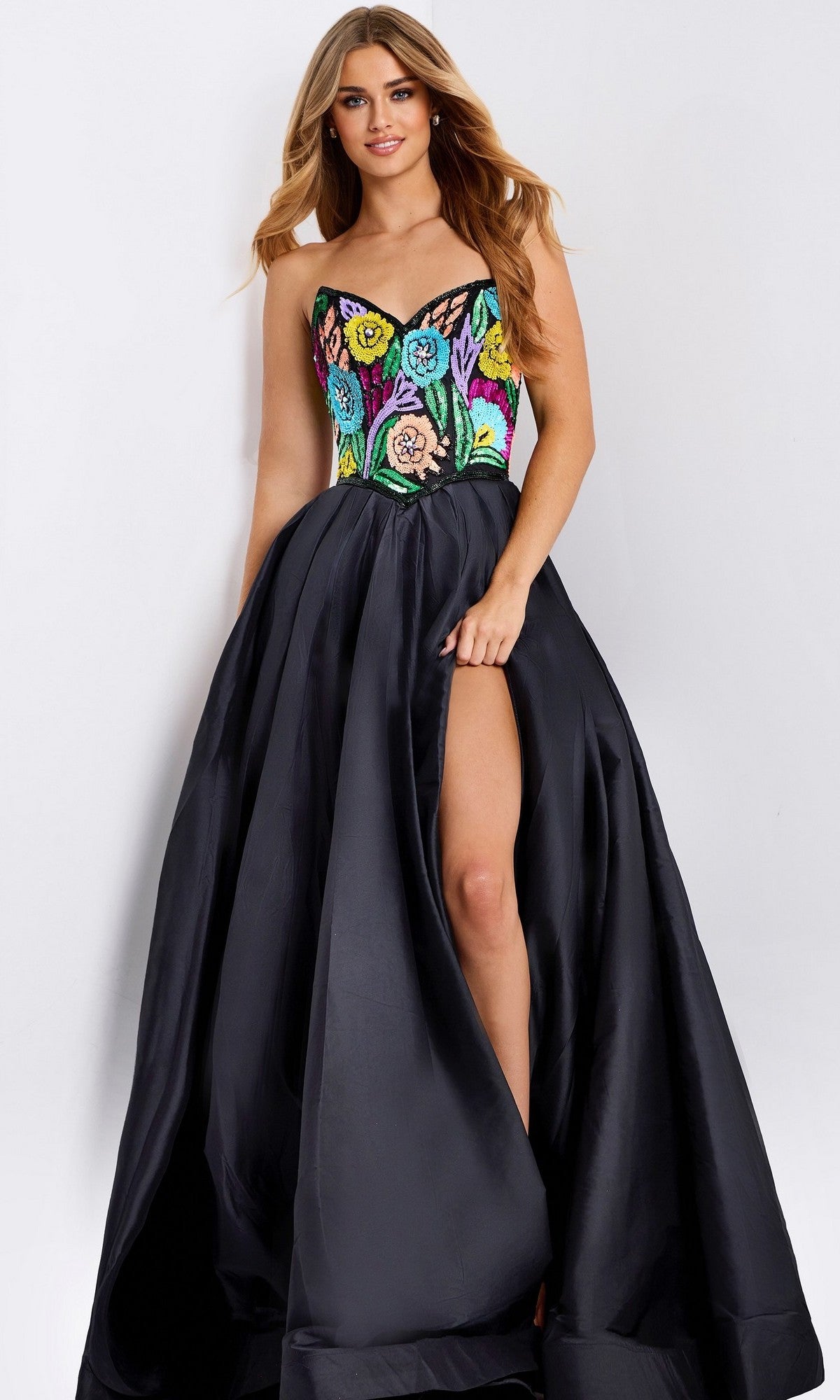 A woman wears the Jovani 49233 long prom dress, featuring a strapless floral-beaded bodice and a black satin A-line skirt with a high slit. She stands against a plain light background.